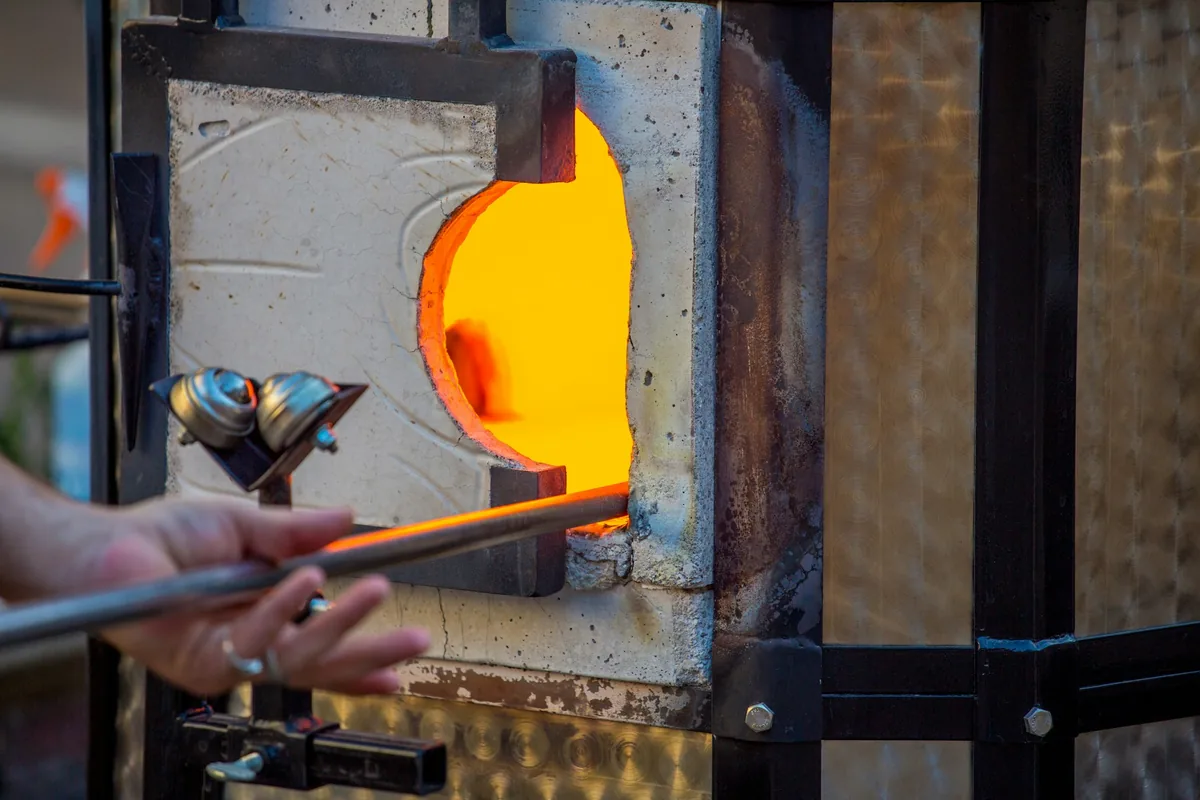 Boca de un horno cerámico abierta durante la subida de temperatura, con el interior incandescente y una herramienta metálica ante la abertura